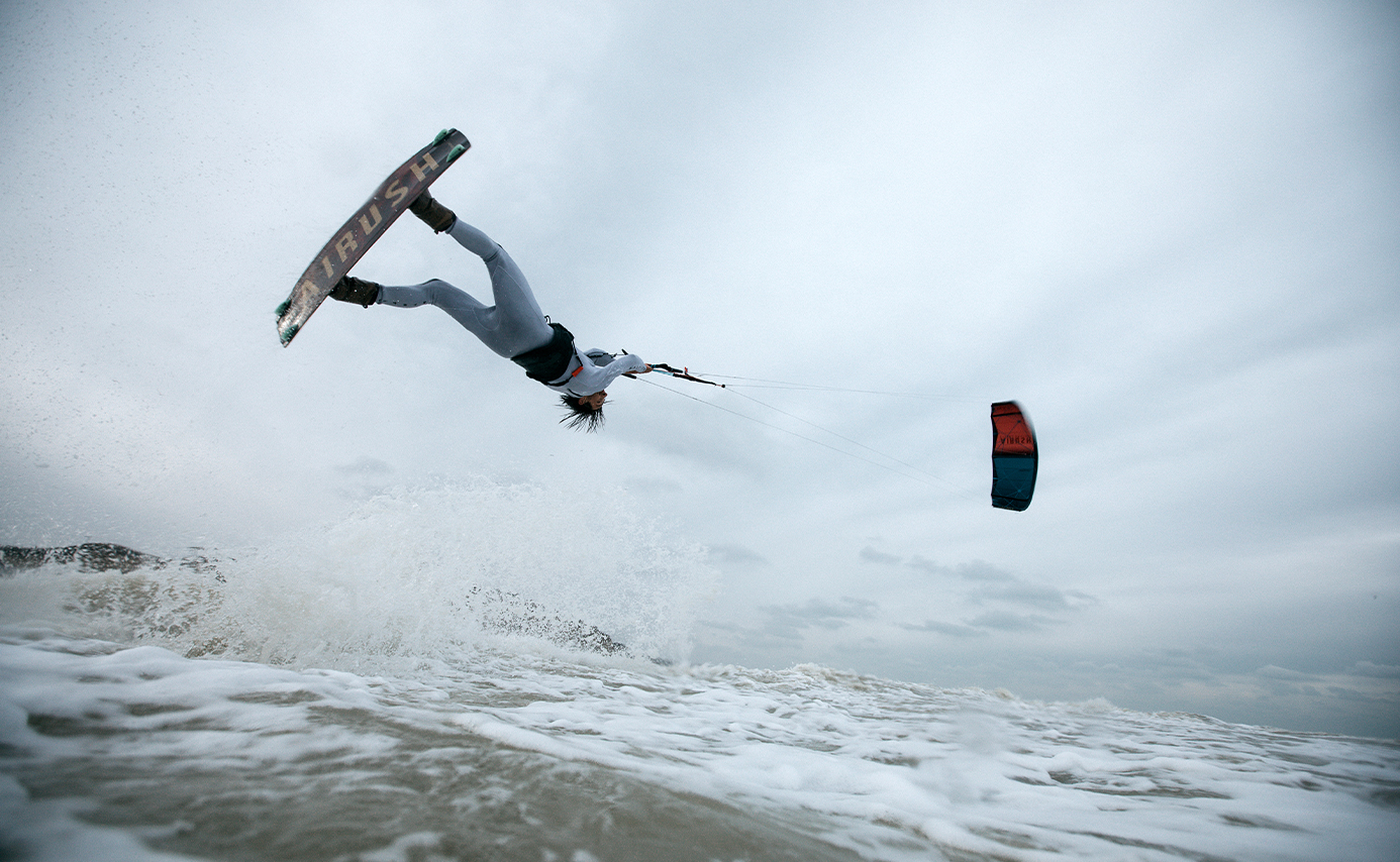 Kitesurfer kopfüber hoch über dem Wasser im Sprung, der Kite seitlich versetzt